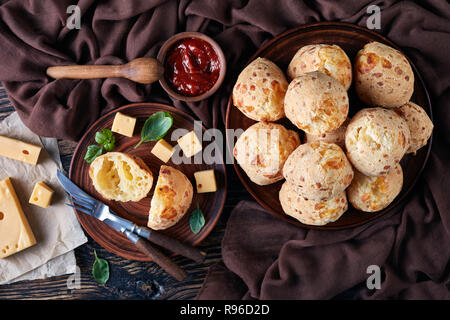 Ansicht von oben von Gougeres, Käse Puffs Kugeln auf einem Steingut Teller. Traditionelle französische Käse choux Brötchen. braun Tuch, Käse und Tomaten Soße auf einer Stockfoto