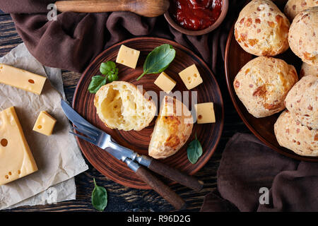 Ansicht von oben von Gougeres, Käse Puffs Kugeln auf einem Steingut Teller. Traditionelle französische Käse choux Brötchen. braun Tuch, Käse und Tomaten Soße auf einer Stockfoto