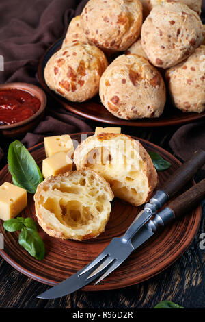 Gougeres, Käse Puffs Kugeln in der Hälfte auf einem Steingut Teller geschnitten. Klassische französische Käse choux Brötchen. braun Tuch, Käse und Tomaten Sauce auf einem alten Holz Stockfoto