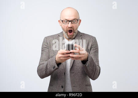 Fassungslos Mann bekommt schlechte Nachrichten auf Smart Phone, blickt mit Angst Ausdruck am Bildschirm, Stockfoto