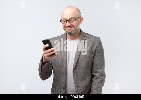 Reifen europäischen kaukasischen Mann Aufmerksam schauen mit Lächeln an den Bildschirm des Smartphones hält er Stockfoto