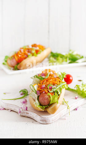 Hot Dog mit Gurke, Karotte, Tomate und Salat auf Holz- Hintergrund. Fast food Menü. Stockfoto