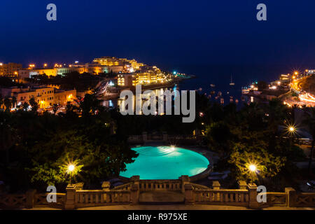 Blick auf St. George's Bay Seafront Lichter in der Nacht, mit einem blauen Luxus Swimmingpool und Boote und Yachten vor Anker. St. Julian's (San Giljan), Central Region, Malta. Abend in Paceville entfernt. Stockfoto