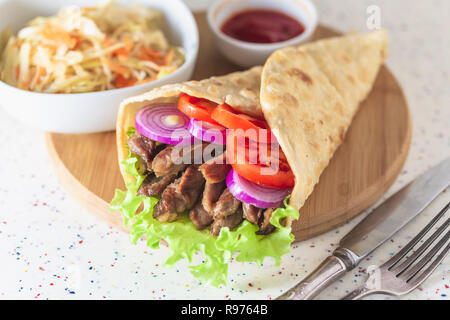 Handgefertigte Döner liegt auf dem weißen Tisch aus Kunststein. Shawarma auf dem hölzernen Schneidebrett mit Hühnerfleisch. Stockfoto