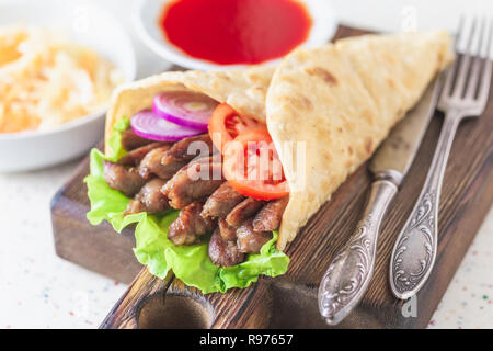 Handgefertigte Döner liegt auf dem weißen Tisch aus Kunststein. Shawarma auf dem hölzernen Schneidebrett mit Hühnerfleisch. Stockfoto