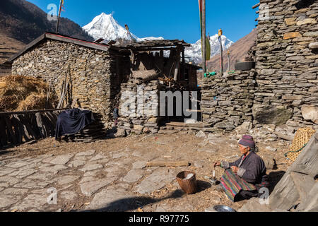 Die ethnisch tibetischen Dorf Lho in der Manaslu Region der Nepal Himalaya. Tibetischen Frau sitzt das Weben in Vordergrund. Stockfoto