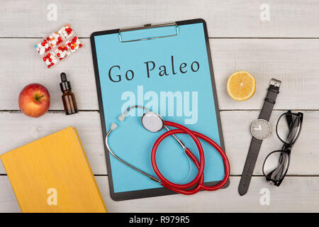 Tiermedizin und Diät Konzept - Zwischenablage mit dem Text "Go Paleo', Pillen, Früchte, Stethoskop, Buch, Brillen und Uhren auf weißem Holz- Hintergrund Stockfoto