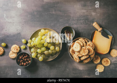 Wein Snack. Käse, Trauben, Nüsse, Käse, Cracker Kekse, Waben mit Messer über dunkle Textur Hintergrund. Flach, Raum Stockfoto