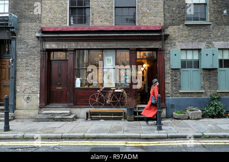 Frau in orange Mantel vorbei Antik Shop mit dem Fahrrad auf Fournier Street in der Nähe von Spitalfields Market im East End von London UK KATHY DEWITT Stockfoto