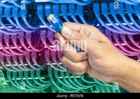 Hand, die Netzwerkkabel auf dem Switch Hub im Server raum Hintergrund Stockfoto