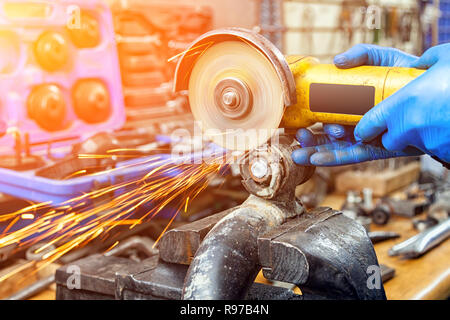 Eine Nahaufnahme von einem Automechaniker mit einem Metall Grinder ein Auto silent Block in einen Schraubstock in einer Werkstatt zu schneiden, helle Blitze fliegen in verschiedenen dire Stockfoto