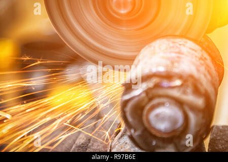 Eine Nahaufnahme von einem Automechaniker mit einem Metall Grinder ein Auto silent Block in einer Werkstatt zu schneiden, helle Blitze fliegen in verschiedene Richtungen. Werde Stockfoto