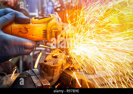 Nahaufnahme eines Mannes Sägen von Metall mit einer Handkreissäge auf einem Holztisch, helle Blitze fliegen in verschiedenen Richtungen, im Hintergrund Tools für Stockfoto