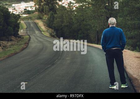 Active Senior Mann stand auf der einsamen Straße zwischen Bergen. Ältere Menschen rücken auf einsamen Highway Stockfoto