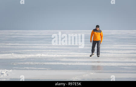 Junge Mann in einem orange Sweatshirt allein Schlittschuhen auf dem Eis eines zugefrorenen Meer Bay Stockfoto