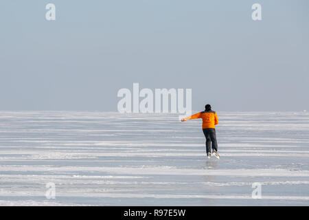 Junge Mann in einem orange Sweatshirt allein Schlittschuhen auf dem Eis eines zugefrorenen Meer Bay Stockfoto
