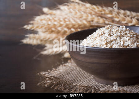 Haferflocken oder Haferflocken in der Schüssel und goldenen Weizenähren auf Holzbrett. Nahaufnahme, horizontal. Das gesunde Essen, veganes Essen Konzept. Stockfoto