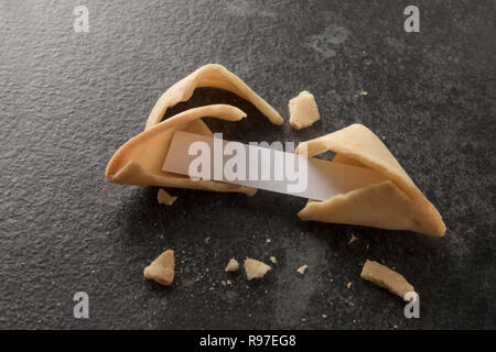 Chinesische Glückskekse, eines mit leerem Papier Slip für die Vorhersage auf dunklem Schiefer Hintergrund mit Kopie Raum gerissen ist Stockfoto