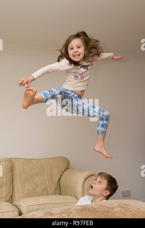 Kinder, Bruder und Schwester springen über auf Möbel, Tauchen und Springen, hyperaktiv, viel Energie, die zusammen spielen Stockfoto