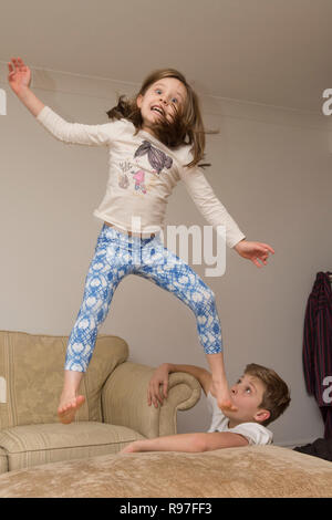 Kinder, Bruder und Schwester springen über auf Möbel, Tauchen und Springen, hyperaktiv, viel Energie, die zusammen spielen Stockfoto