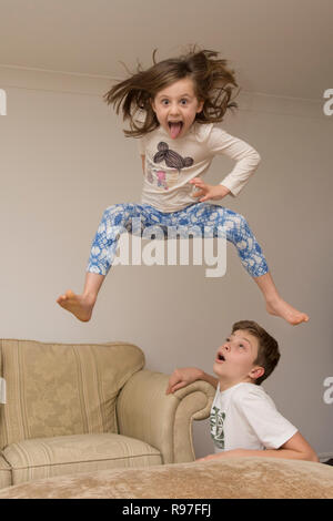 Kinder, Bruder und Schwester springen über auf Möbel, Tauchen und Springen, hyperaktiv, viel Energie, die zusammen spielen Stockfoto