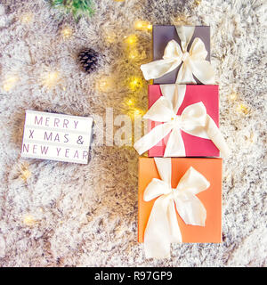 Draufsicht auf die Zusammensetzung der beleuchteten Kasten mit Frohe Weihnachten und neues Jahr wünsche und Geschenke in bunten festliche Verpackung mit Bogen unter xsmas Baum gebunden Stockfoto