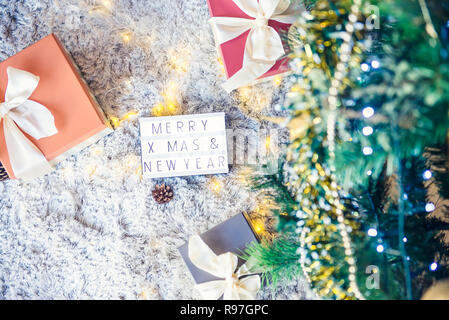 Draufsicht auf die Zusammensetzung der beleuchteten Kasten mit Frohe Weihnachten und neues Jahr wünsche und Geschenke in bunten festliche Verpackung mit Bogen unter xsmas Baum gebunden Stockfoto
