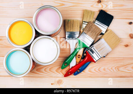 Vier offene Farbdosen mit Bürsten auf natürliche Holz- Hintergrund. Gelb, Weiß, Rosa, Türkis Farben. Sanierungskonzept. Stockfoto