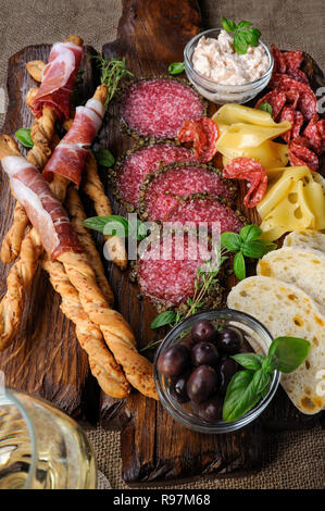 Teller für Antipasti Snacks mit Salami, Brot Sticks (Grissini) mit Schinken, Oliven und Käse Paste auf der Holzoberfläche gewickelt Stockfoto