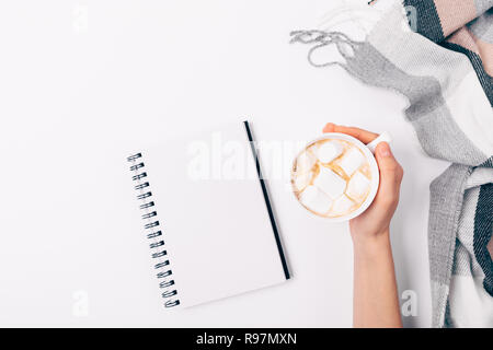 Flach hand Komposition von weiblichen Holding Becher Kaffee mit Marshmallows in der Nähe von offene leere Notepad und karierten Plaid auf weißem Hintergrund, Ansicht von Stockfoto