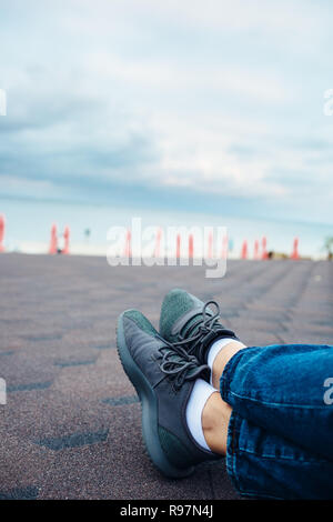 In der Nähe der weiblichen Beine in Jeans und Turnschuhe. Junge Frau sitzt auf Dach über dem Strand. Stockfoto