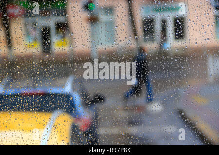 Regen vor dem Fenster auf dem Hintergrund der Stadt. Tropfen Wasser fällt auf Glas bei Regen. Passanten pass Straße im Regen. Wassertropfen über Stockfoto