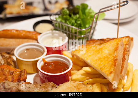 Selektive konzentrierte Nahrung, Pommes Frites und gebackene Butter Brot Abstellgleis Steaks und Würstchen Sortiment mit verschiedenen Saucen und frisches Gemüse in whit Stockfoto