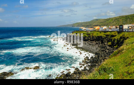 Rocky schwarz Küste der Azoren mit Absturz blauen Wellen und ein kleines Dorf an einem wunderschönen sonnigen Tag. Stockfoto