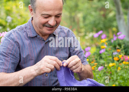 Alte schöner Mann an seinem Sommergarten sitzen und die Stricknadeln. Stockfoto