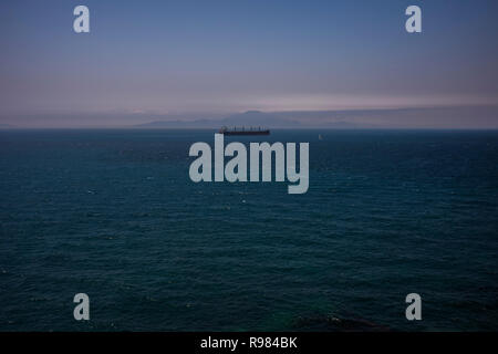 Ein Frachtschiff fährt die Straße von Gibraltar, wie die Berge von Marokko, Afrika von Gibraltar aus gesehen an einem klaren Tag. Stockfoto