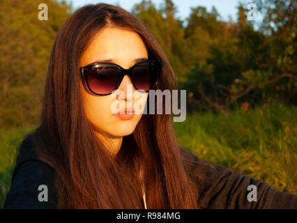 Das Mädchen in der Brille sitzt in der Mitte des Waldes und aalt sich in der Sonne. Ohne Behandlung. Stockfoto