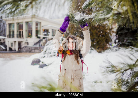 Schönen jungen kaukasischen Frau Freude Glück Lächeln spielen mit Schnee in der Nähe von einem nadelwald Baum in einer verschneiten Park. Stockfoto