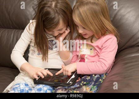 Zwei junge Schwestern spielen auf einem Tablet-PC, digitale Gerät, iPad, elektronische Medien, entspannt auf einem Sofa. Stockfoto