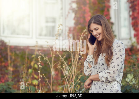 Lächelnden jungen Frau Plaudern auf einem mobilen im Herbst vor dem Weißen Haus mit bunten Kriechgang lächelnd Stockfoto