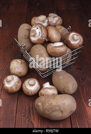 Ein metalldraht Korb mit Kartoffeln und Pilze auf einem Holztisch gefüllt. Stockfoto