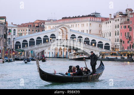 Venedig, Italien, 21. März 2018: Venezianische Gondoliere, Touristen auf der Gondel am Grand Canal und die Rialto Brücke im Hintergrund Stockfoto