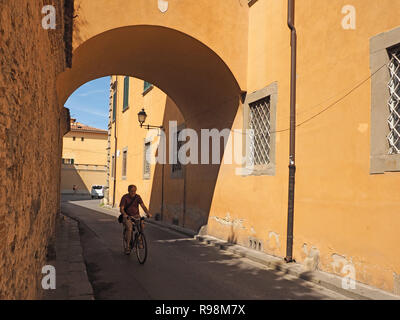 Radfahrer fährt oben sitzen und betteln Zyklus im Schatten auf einer menschenleeren Stadt Straße durch gewölbte Tunnel zwischen Ocker Stadtzentrum Gebäude in Pisa, Italien Stockfoto