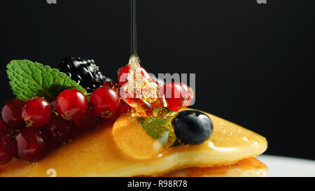 Stapel von frischem flauschige Pfannkuchen auf die Oberseite mit Waldbeeren auf dem Teller dekoriert und Gießen Honig Sirup. Leckere, gesunde amerikanisches Frühstück. Frische Backwaren Konzept Stockfoto