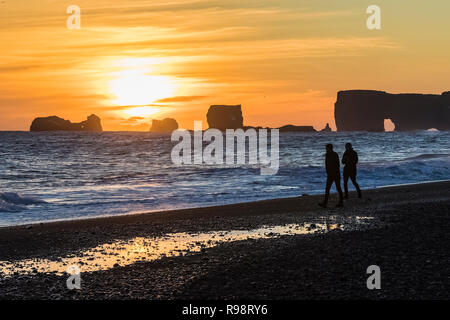 Wellen, die am Sonnenuntergang mit Dyrhólaey, ein Felsen mit einem Bogen, der in der Entfernung entlang der schwarze Sandstrand in der Nähe des Dorfes Vik im Winter in Island Stockfoto