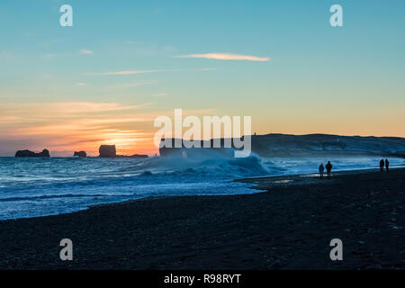 Wellen, die am Sonnenuntergang mit Dyrhólaey, ein Felsen mit einem Bogen, der in der Entfernung entlang der schwarze Sandstrand in der Nähe des Dorfes Vik im Winter in Island Stockfoto