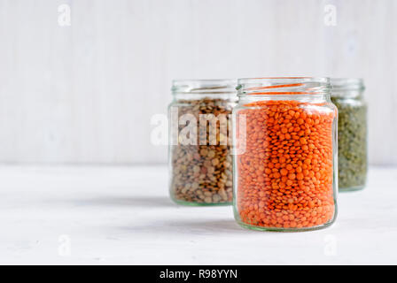 Rot oder orange Linsen in einem gläsernen Gefäß mit Gläser grüne Linsen hinter in einer gesunden Diät- oder vegetarische Küche Konzept Stockfoto