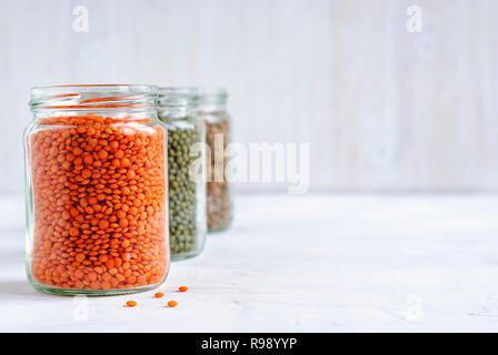 Rot oder orange Linsen in einem gläsernen Gefäß mit Gläser grüne Linsen hinter in einer gesunden Diät- oder vegetarische Küche Konzept Stockfoto