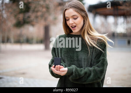Schöne junge Dame im stilvollen Outfit suchen bei der Hochzeit Ring in Feld beim Stehen auf verschwommen Stockfoto