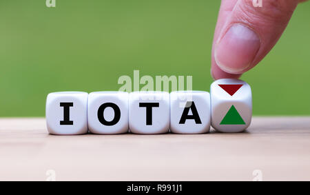 Hand dreht einen Würfel und verändert die Richtung, in die sich ein Pfeil symbolisiert, dass der Wert der crypto Währung IOTA wird (oder umgekehrt) Stockfoto